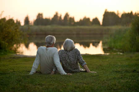 Elderly couple sits on the shore of a lake. Rear view.の写真素材