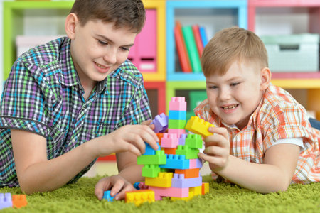 brothers playing with colorful plastic blocks in roomの写真素材