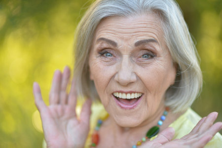 Close up portrait of happy older woman standing outside in summerの写真素材