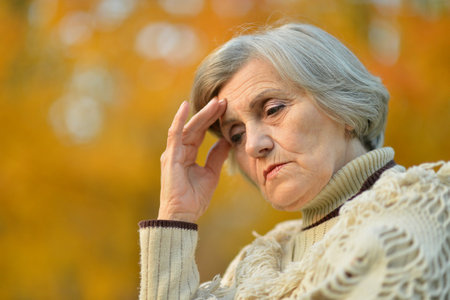 Sad senior woman with headache in parkの写真素材