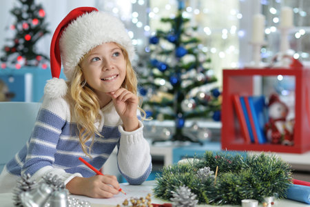 Little girl writing letter to santa in santa hat at homerの写真素材