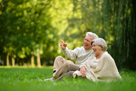 Nice mature couple sitting on green grass in summer park.の写真素材
