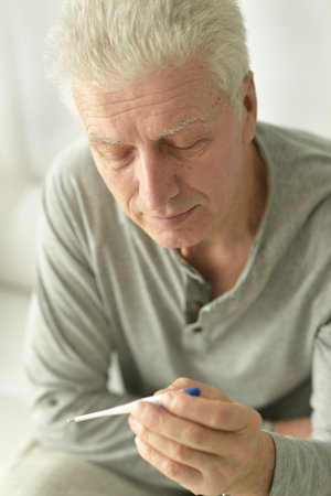 A sick elderly man sits on his bed and checks his body temperature.の写真素材