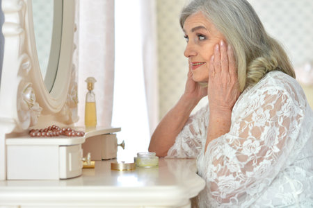 Smiling senior woman doing makeup in front of mirror at homeの写真素材