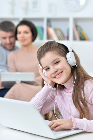 Cheerful little girl using a laptop at home with her parents in the background.の写真素材