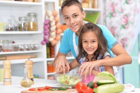 Cute little brother and sister preparing salad together at kitchenの写真素材