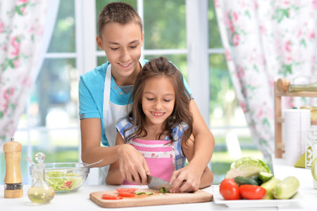 Cute little brother and sister preparing salad together at kitchenの写真素材