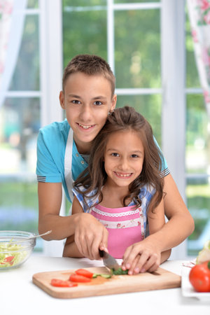 Cute little brother and sister preparing salad together at kitchenの写真素材
