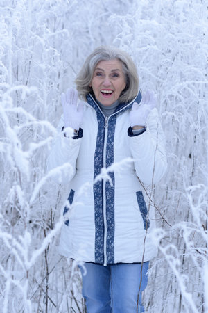 Beautiful elderly woman posing in a snowy winter parkの写真素材