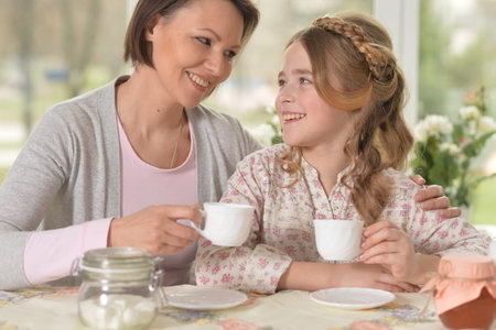 Happy mom and daughter drinking tea at homeの写真素材