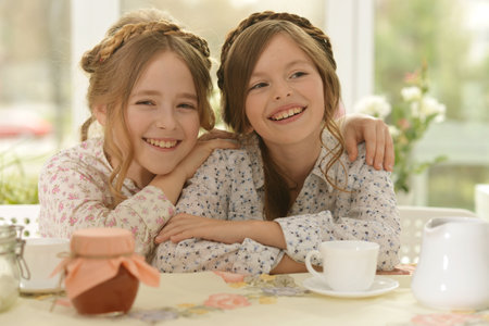 Portrait of two smiling little girls drinking tea at homeの写真素材