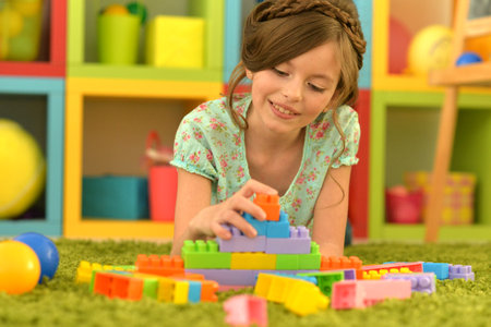Portrait of cute girl playing with colorful plastic blocks in roomの写真素材