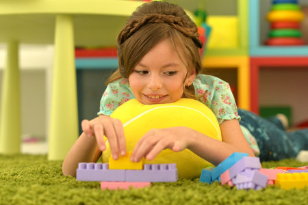 Portrait of cute girl playing with colorful plastic blocks in roomの写真素材