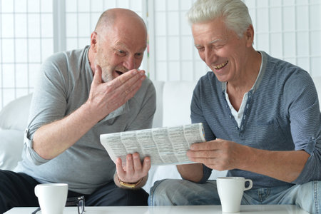 Two old men sitting at table and discussing newsの写真素材