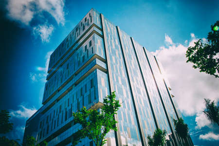 Corporate building with walls made of glass windows with a blue sky with clouds in the background.の写真素材