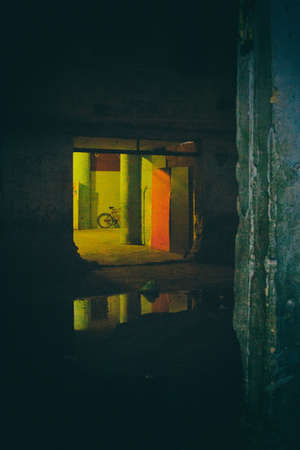 An old huge window in now used as entrance in a condemned abandoned building used as home by social housing movement. A giant puddle on the dirty floor reflects the environment. No people.の写真素材