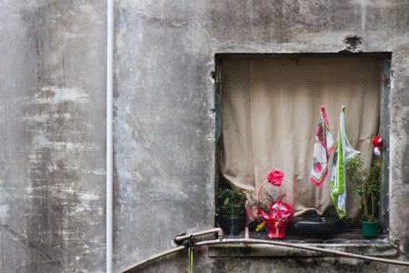 View from a window with a creamy closed curtain of an eroded building with a pink flower and a Brazilian flag hanged on the outside.の写真素材