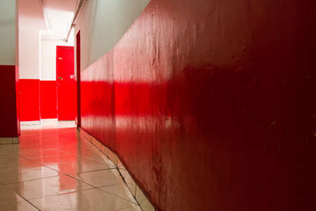 Red and white corridor with red door and the sun light at the end of it. No people.の写真素材