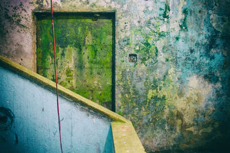 Yellow worn door in from of a concrete staircase in an abandoned building with eroded timeworn blue walls with a red electric wire coming down from above. No people.の写真素材