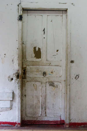 Warn white door with the number 1 on it with cracked white walls and decayed red floor.の写真素材