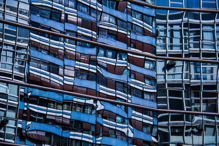 Home building reflected on a commercial building made of blue glass walls.の写真素材