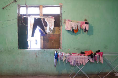 Cracked walls and floor with drying clothes near a window and a TV antenna of a decayed occupied building by a social housing movement.の写真素材