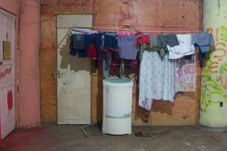 Washing machine and bed sheets and clothes hanged to dry on the outside of an apartment with worn wooden planks and cracked walls.の写真素材