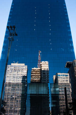 A modern office tall building with an illumination pole in front reflects the environment in their blue windows made of glassの写真素材