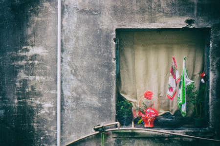 View from a window with a creamy closed curtain of an eroded building with a pink flower and a Brazilian flag hanged on the outside.の写真素材