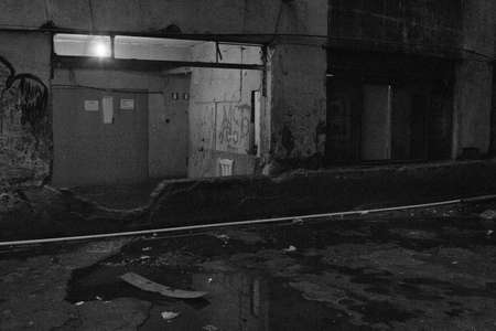Huge window in now used as entrance in a condemned abandoned building used as home by social housing movement. A puddle on the dirty floor reflects the environment. Black and white. No people.の写真素材