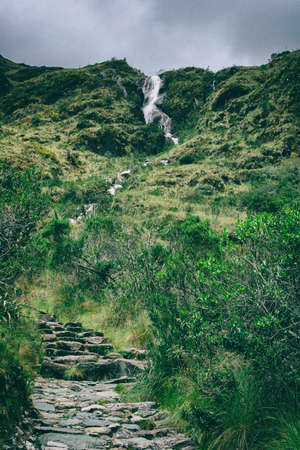 Surrounded by wild and ancient forest a waterfall on the stone paved path Inca Trail on the way to Machu Picchu, Peru.の写真素材