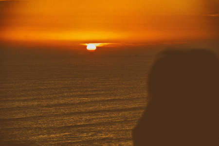 Silhouette of a person looking at the sunset in the ocean with an island. Beautiful wallpaper.の写真素材