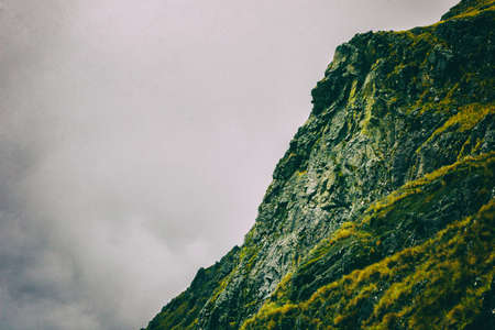 Detail of the side of a rocky mountain with green grass and intense clouds formation on the background. Cool wallpaper image. Peru. South America. No people.の写真素材