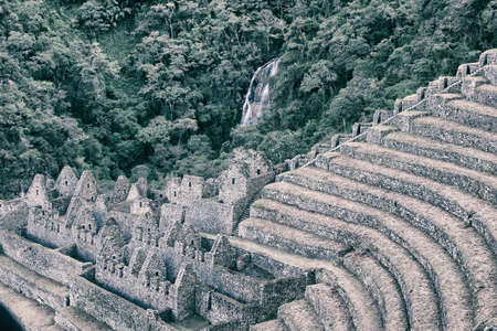 Inca Trail sightseen of an ancient stone ruin town with agriculture terraces covered by grass with green wild forest and waterfall on the mountain on the background. Beautiful wallpaper.の写真素材