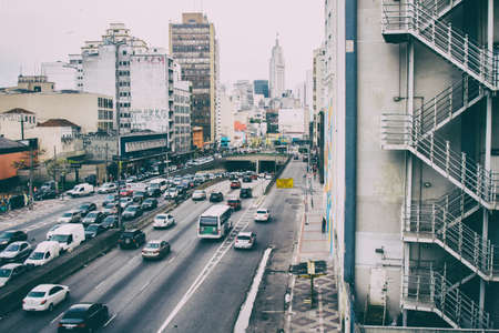 Crowded avenue view from high with in the foreground a business building external emergency stairs and the skyline of the metropolis in the background.のeditorial素材