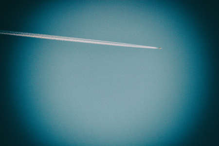 Wallpaper background of an airplane trace in the blue sky. Vignette effect.の写真素材