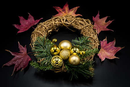 Holidays wallpaper background of twig Christmas wreath with golden balls and decorations, green branches and red dried leaves on black background.の写真素材
