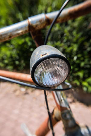 Vertical image of a worn rusty brown vintage bicycle with big front light and green leaves wall on the background.  .の写真素材