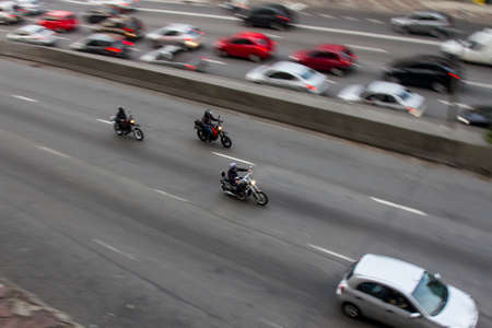 Pan shoot of motorcycles at high speed on an avenue in downtown from a nearby building with slower...