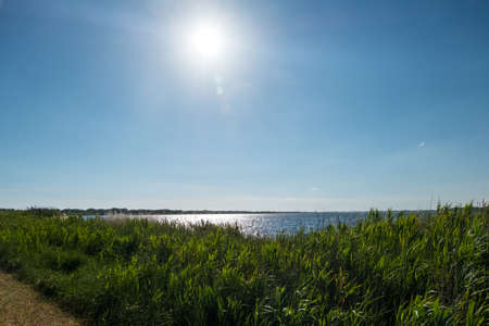 Wallpaper background of nature with bright sun in blue sky and a lake with calm water on the landscape background.の写真素材