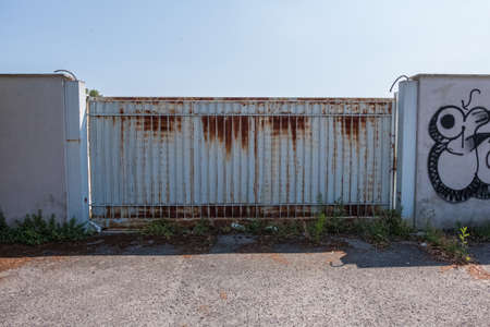 Industrial grungy wallpaper background of an automatic white metallic gate with rust on a summer day with blue sky in the background. No people.の写真素材
