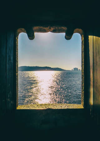 Landscape view of the sun reflection over the sea water with mountains on the background from an ancient stone window. No people.の写真素材