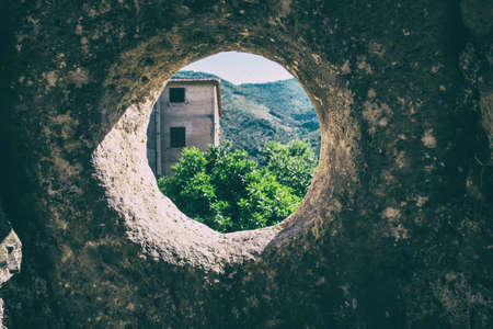 Wallpaper background of a round window of an ancient wall with landscape of mountains, nature a an...