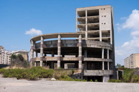Huge multi floors concrete structure of abandoned building with stairs surrounded by grass and trees with blue sky in the background. Architecture detail. No people.の写真素材
