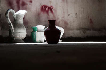 Wallpaper background of old vintage worn green ceramic water vases on the floor near a window with day light from the outside. No people.の写真素材