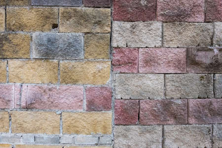 Wallpaper background texture of a wall made of big colorful red, grey, yellow and white worn bricks. Grunge background.の写真素材