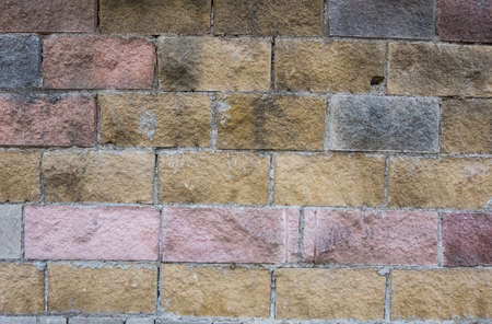 Wallpaper background texture of a wall made of big colorful red, grey, yellow and white worn bricks. Grunge background.の写真素材