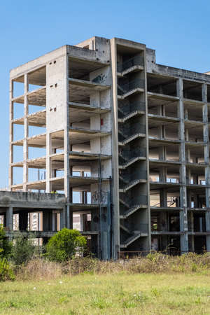 Huge multi floors concrete structure of abandoned building with stairs surrounded by grass and trees with blue sky in the background. Architecture detail. No people.の写真素材