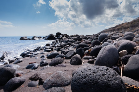 Black volcanic stones on the beach shore of Santoriniの写真素材