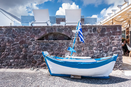 Wooden small blue and white boat in front of a wall of Santorini.の写真素材